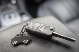 Como saber se um veículo está quitado: a chave de um carro possui um chaveiro de automóvel em miniatura. Ambos estão em cima de uma superfície preta dentro do automóvel.