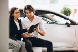 Homem e mulher sentados dentro de uma loja de veículos com documento nas mãos (seguro auto)