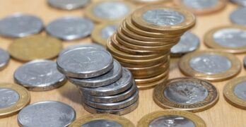 Nota Fiscal Paulista: diversas moedas de cinquenta centavos e um real estão espalhadas e, algumas, empilhadas.
