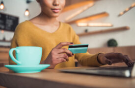 Cartão de crédito: uma mulher está mexendo no notebook e segurando um cartão. Ao lado há uma xícara.