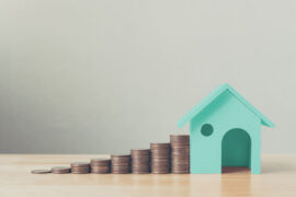Financiamento de imóvel: imagem mostra uma miniatura de residência ao lado de oito pilastras de moedas.