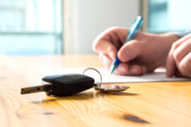 Refinanciar carro: uma pessoa assina um documento, e ao lado há a chave de um veículo