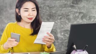 cartão: mulher em frente ao computador segurando um cartão em uma mão e uma folha na outra