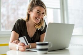 limite do cartão de crédito: mulher em frente ao computador segurando um cartão de crédito