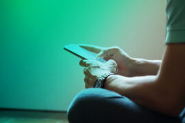 Pix Parcelado: um homem está de camiseta verde e calça jeans, sentado e mexendo no celular. Não é possível ver seu rosto.