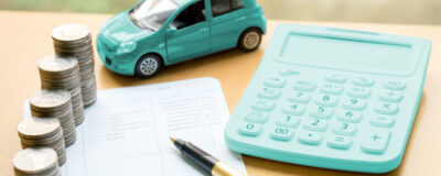 Financiamento de carro: um veículo em miniatura está ao lado de uma calculadora, um contrato, algumas moedas e uma caneta.