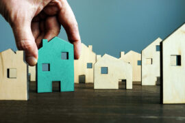 Financiamento de casa: uma pessoa insere a miniatura de uma residência entre outras miniaturas de diversas formas.