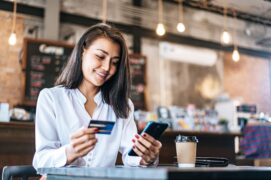 mulher segurando cartão e celular (senha do cartão Itaú)