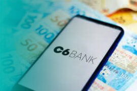 limite do cartão de crédito: celular mostrando o logo do C6 Bank e notas de cinquenta e cem reais atrás