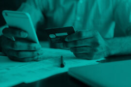 Um homem segura um cartão de crédito com a mão esquerda e, com a outra, mexe no celular.