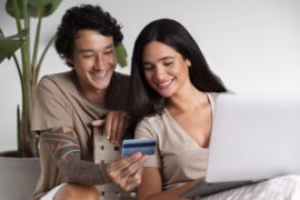 casal segurando cartão e computador (cartão de crédito Sicoobcard)
