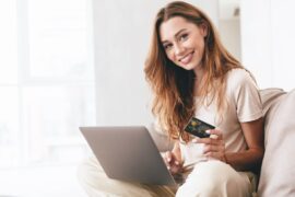 Cartão de crédito: mulher sorrindo segurando cartão em frente ao computador