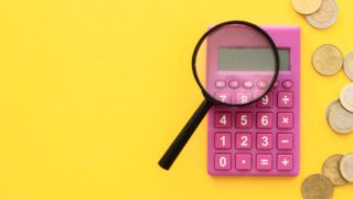 financiamento de veículo: calculadora rosa com lupa sobre ela e moedas ao lado
