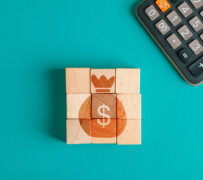 Renda fixa: três peças de madeira, juntas, formam o desenho de um saco de dinheiro laranja com um cifrão. Ao lado é mostrada uma parte de uma calculadora.