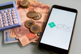 Pix: celular com logo do pix e notas de dez reais, moedas de um real e calculadora atrás