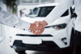 Homens apertando as mãos em frente a um carro (juros de financiamento de veículos)