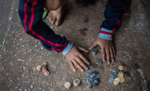 Programa de Erradicação do Trabalho Infantil (PETI): uma criança está ajoelhada no chão, contando moedas.