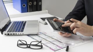 homem usando calculadora e computador (declarar o Imposto de Renda)