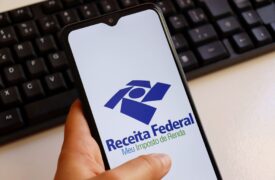 Uma pessoa mexe no celular e, na tela, está o logo da Receita Federal e o nome do aplicativo 