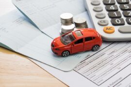Financiamento de veículo no Imposto de Renda: uma miniatura de veículo vermelha está em cima de alguns papéis. Ao lado há moedas empilhadas e uma calculadora.