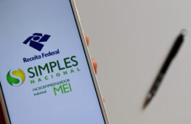 DAS: uma pessoa segura um celular e, na tela, é mostrado o logo da Receita Federal e do Simples Nacional.