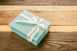 Dia das mães: uma caixa de presente retangular verde, com um laço, está em cima de uma mesa de madeira marrom.