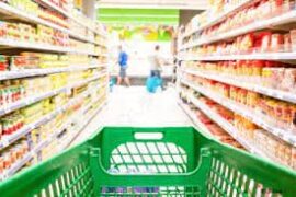 Como economizar na alimentação: um carrinho de supermercado verde está adentrando um corredor com diversos produtos em gôndolas.