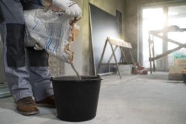 Pessoa despejando cimento em balde (consórcio para construção de imóvel e reforma)