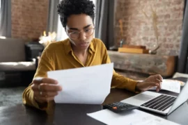 Portabilidade de financiamento: uma mulher avalia um documento, enquanto mexe notebook.