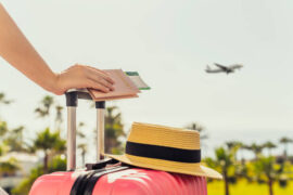Consórcio para viagem: uma pessoa segura o passaporte e apoia a mão em uma mala de rodinhas. Há um avião à frente.
